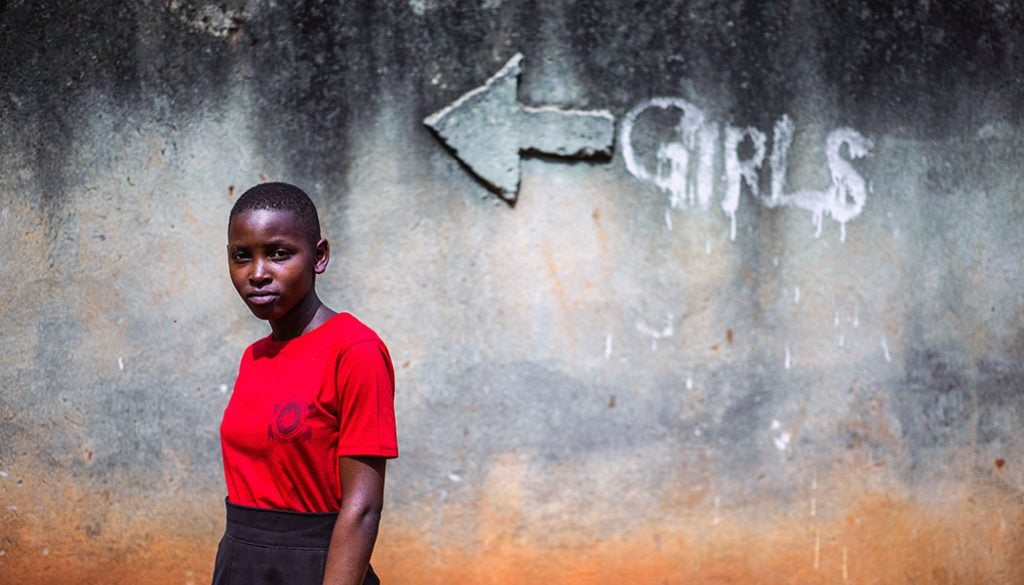 A girl stands in front of a sign that says "girls."