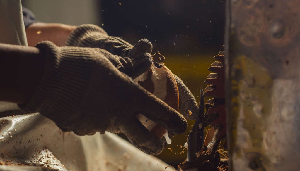 A worker wearing protective gloves cuts the shell off a coconut.