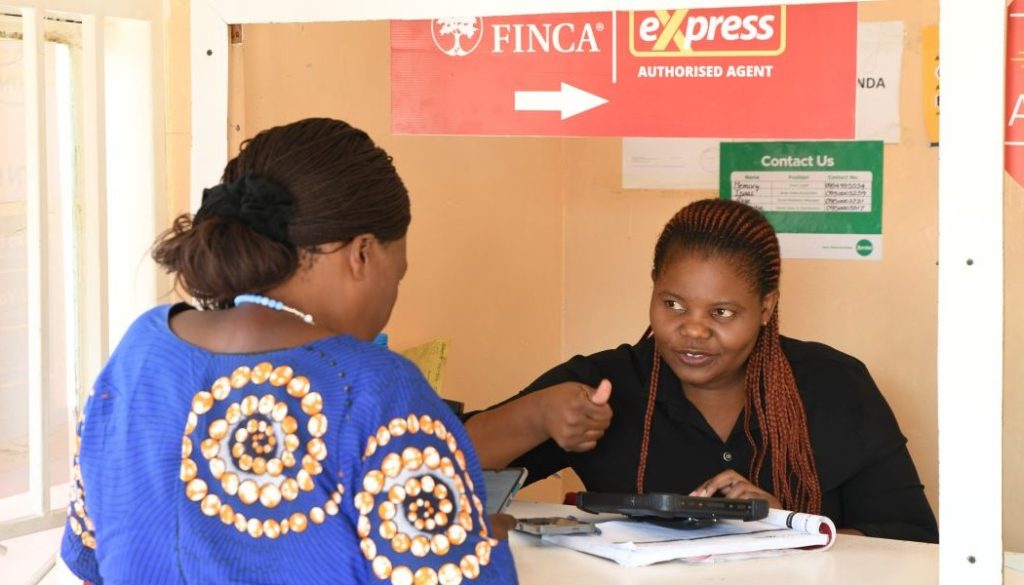 A FINCA banking agent shows a client how to use their thumbprint to complete a transaction.