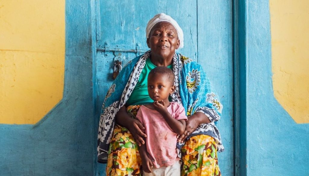 An older woman and a chil in front of their brightly painted house in Kwale, Kenya. Alice Mugugumbi says she greatly benefits from working with FINCA's partner, Kentaste.