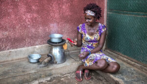 Irene Ahebwa uses a BrightLife stove to cleanly cook a meal and charge her phone.