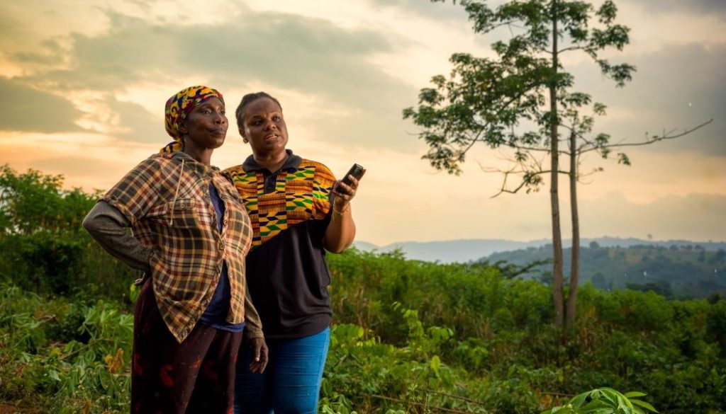 Women wearing color clothing in a field with a tree and landscape in the distance. The women use Ignitia's weather forecasting tool to escape poverty in Ghana.