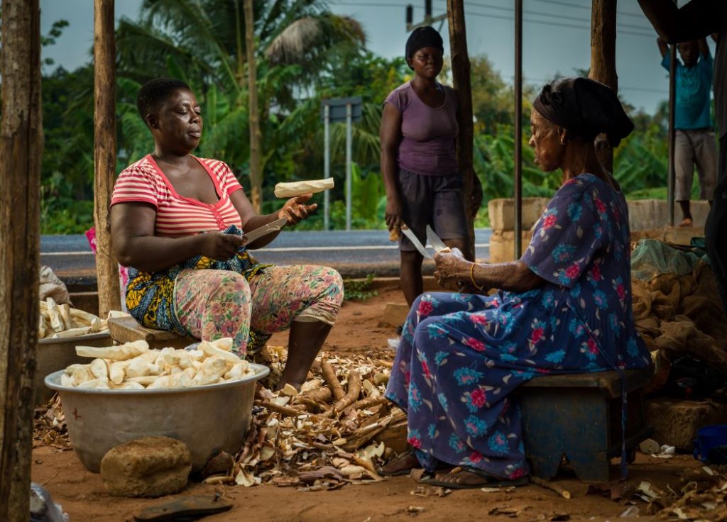 Women sitting and trimming cassava in a roadside stall. The women are seasonal Margaret Terkpertoi's employees.