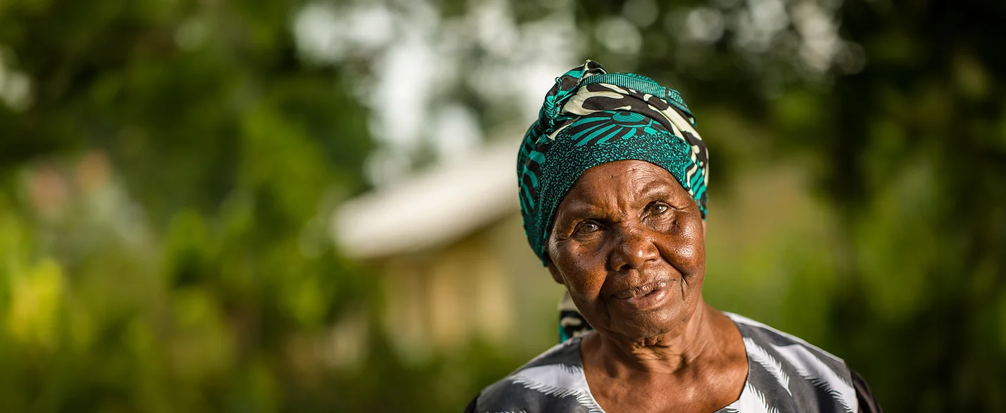 Elderly woman with green headscarf smiling.