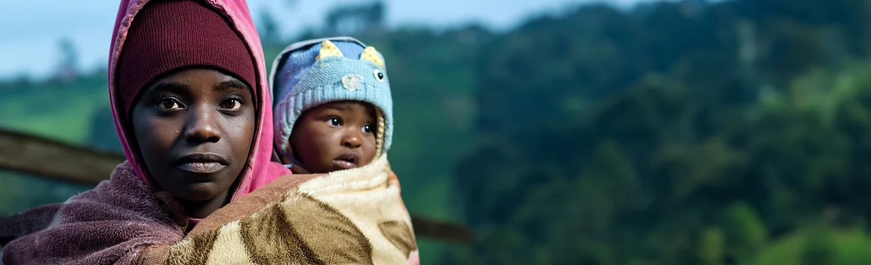 Woman in a pink hoodie holding a baby with a blue hat.