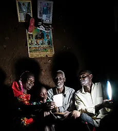 Famille assise ensemble, éclairée par une petite lampe. Cliquez pour en savoir plus sur l'énergie. 