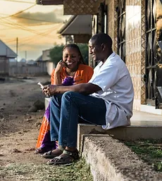 Homme et femme assis sur des marches, souriant et parlant. Cliquez pour en savoir plus sur l'Autonomisation Financière. 