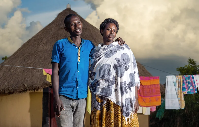 Couple se tenant ensemble devant une maison en chaume avec du linge.